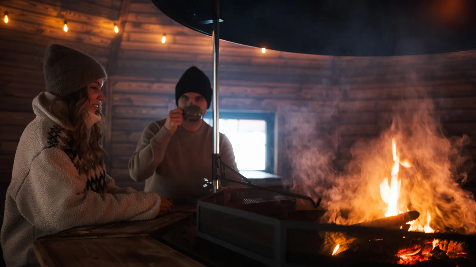 Two guests in winter hats sharing warm drinks beside an open fire in the Hillside kota restaurant